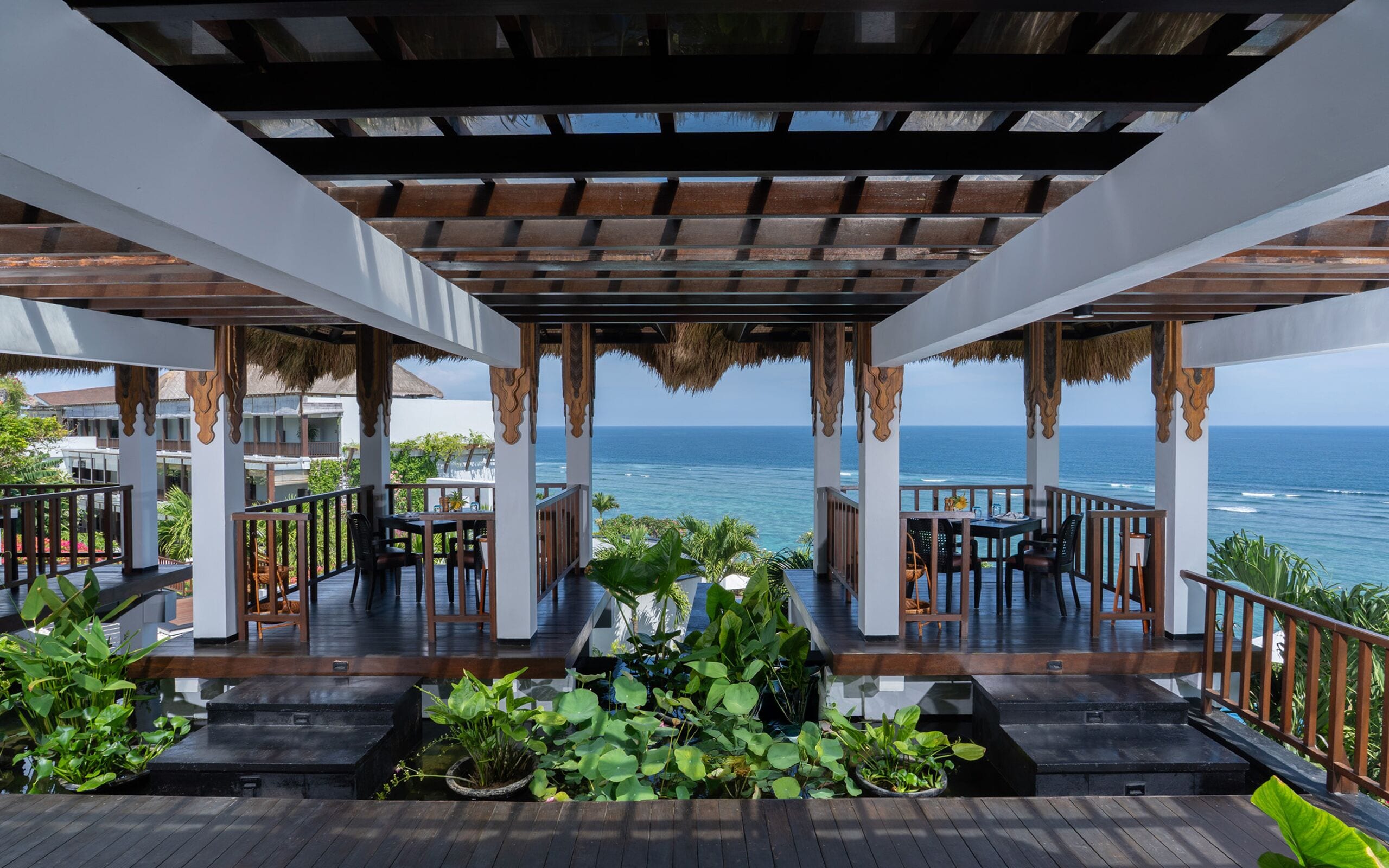 An outdoor terrace with wooden flooring, thatched roof, and a view of the ocean.