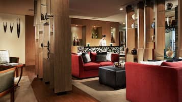 A modern living room with a red sofa, a black ottoman, and a wooden coffee table. There are decorative vases on shelves and a wooden partition with a decorative pattern.