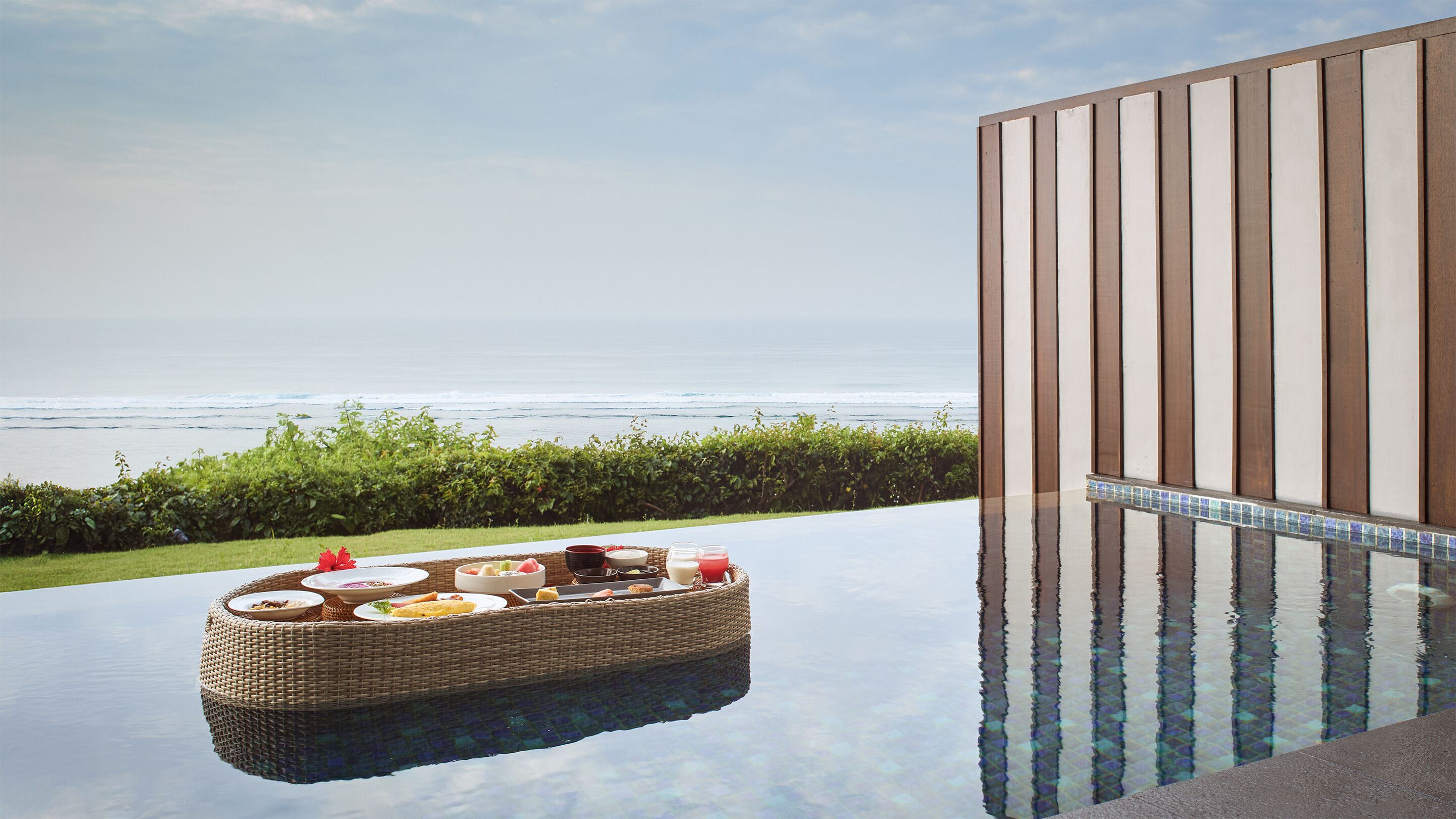 An infinity pool with a wicker lounge chair and a tray of food, overlooking the ocean.