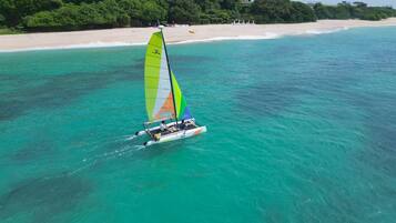 A sailboat on turquoise waters with a beach and greenery in the background.