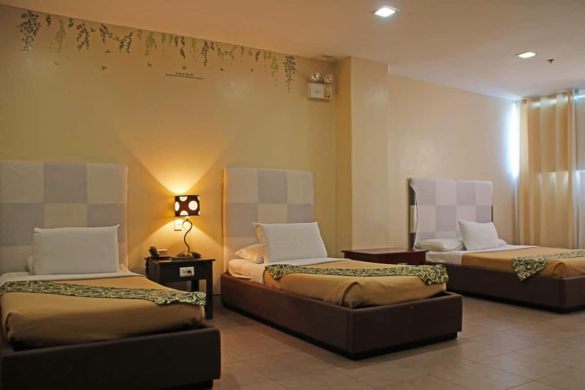 A hotel room with three beds, a nightstand with a lamp, and a wall-mounted air conditioner.