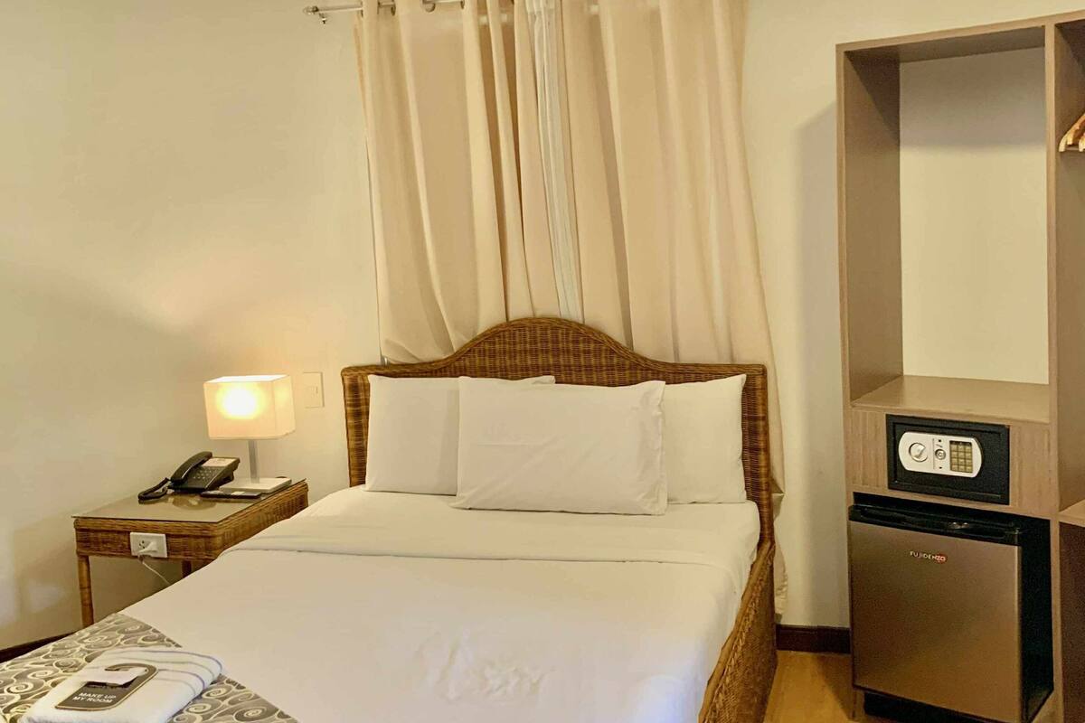 A hotel room with a bed, a bedside table with a lamp, a minibar, and a wardrobe.