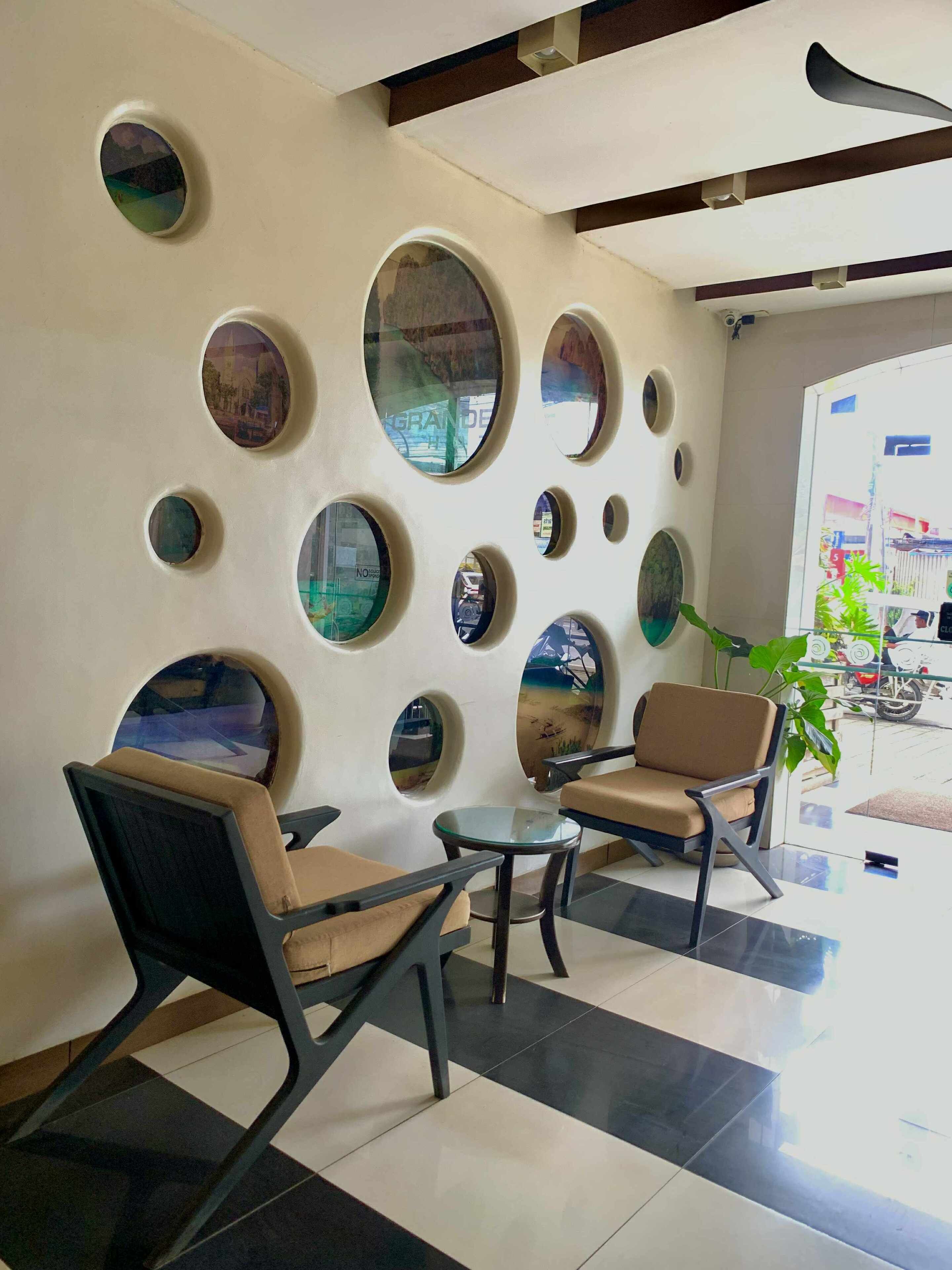 Un hall d’entrée au design moderne, agrémenté de miroirs ronds au mur, de deux fauteuils et d’une table en verre.