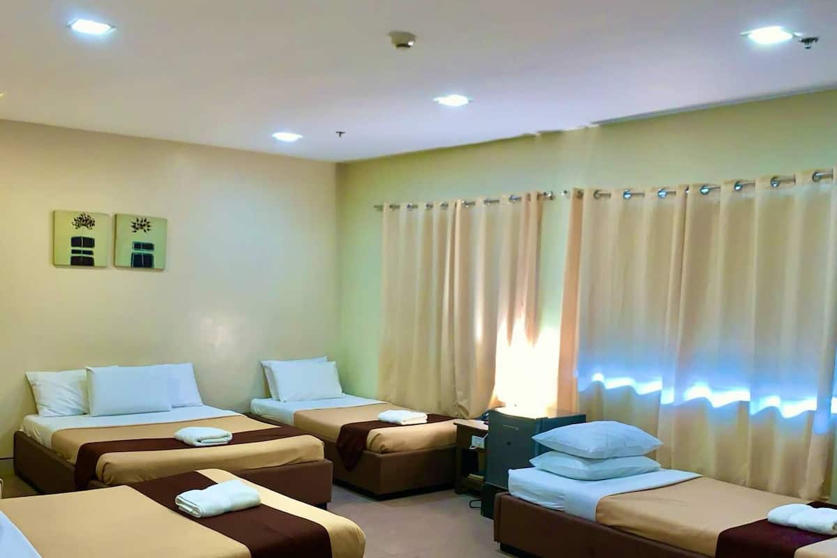 A hotel room with four beds arranged in a U-shape, a desk, and a large window with curtains.
