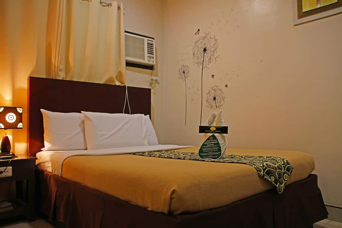 A hotel room with a bed, a nightstand, a lamp, an air conditioning unit, and a wall decoration of dandelions.