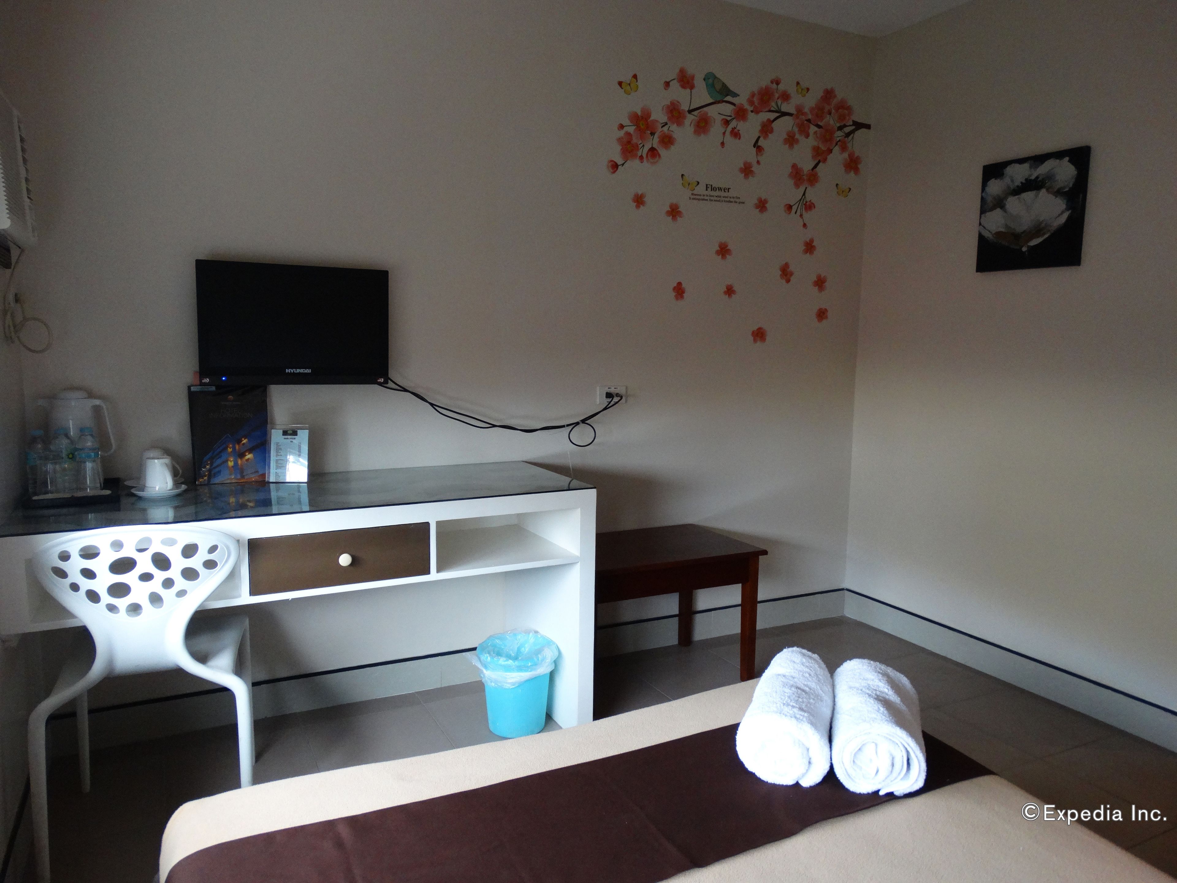 Camera d'albergo con un letto, una scrivania con un computer, una sedia, un tavolino, un cestino e un elemento decorativo a parete.