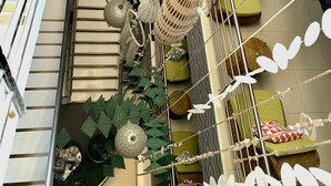 A multi-level atrium with a central staircase, decorative hanging elements, and green upholstered seating areas.