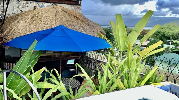 A pool area with a thatched-roof structure, a blue umbrella, and tropical plants.
