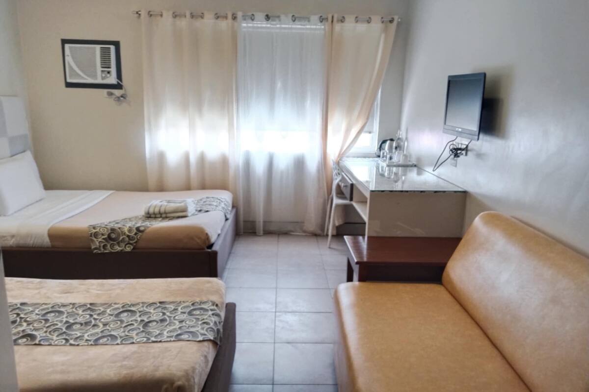 A hotel room with two beds, a desk, a chair, a TV, and a window with curtains.