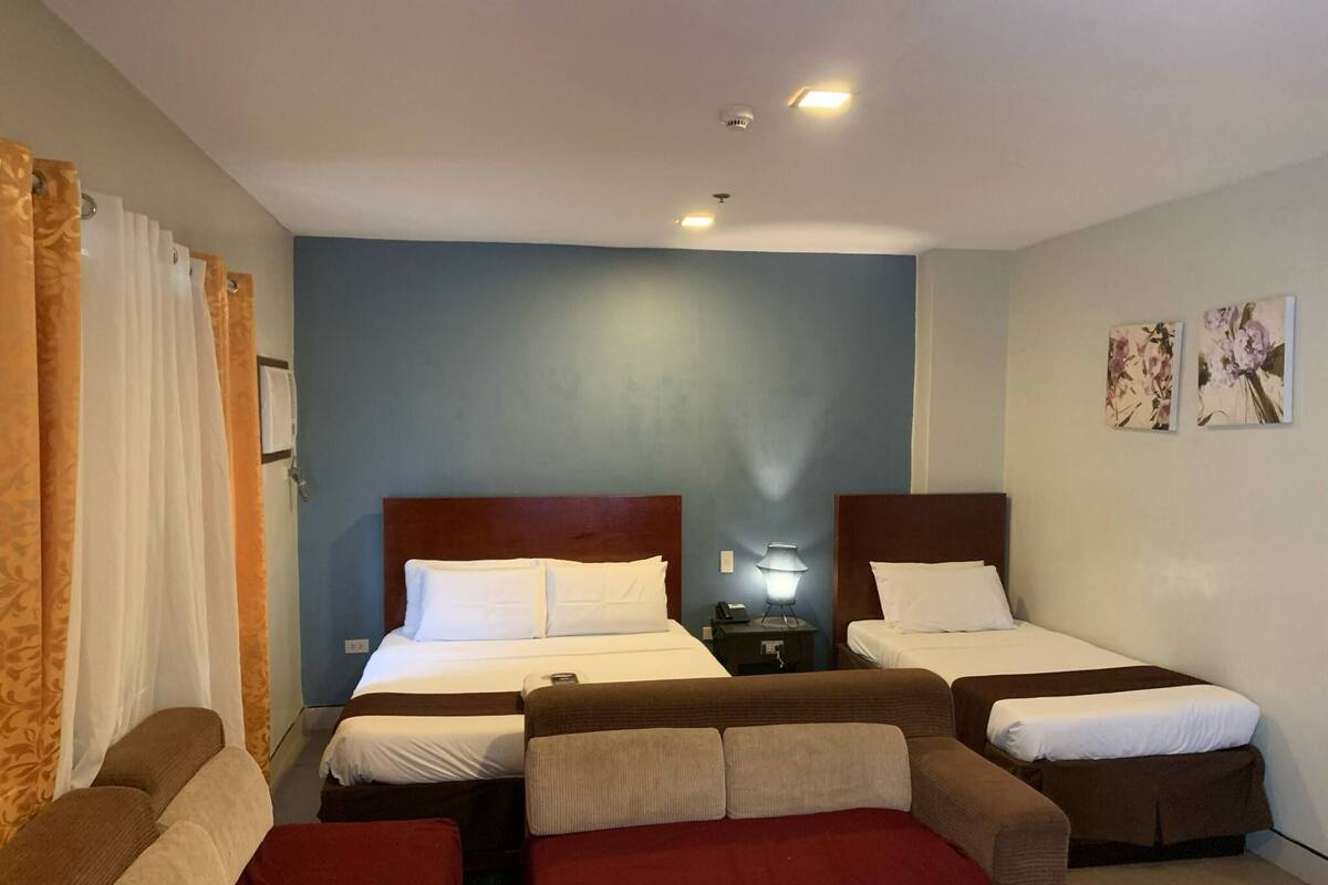 A hotel room with two beds, a nightstand, a lamp, and a red sofa.