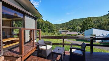 Relax on the deck with wicker chairs and a small table, taking in the view of the lush green landscape and distant hill.