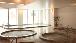 A modern indoor swimming pool area with multiple hot tubs and a large glass window providing natural light. - LiVEMAX RESORT Greenpia Onuma (Mori)