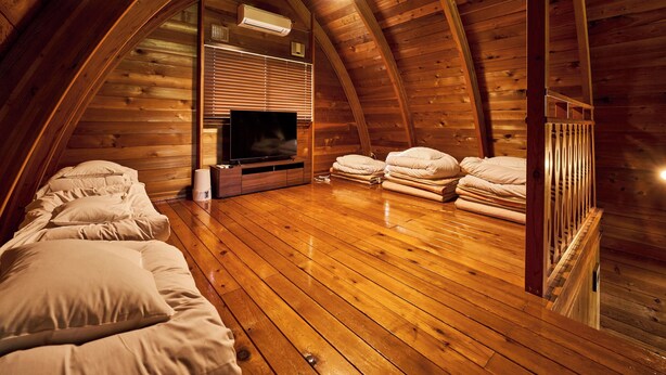 A cozy attic bedroom with wooden walls, a flat-screen TV, and neatly stacked bedding. - LiVEMAX RESORT Greenpia Onuma (Mori)