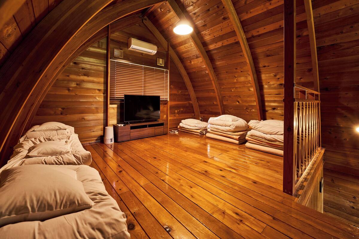 A cozy attic bedroom with wooden walls, a flat-screen TV, and neatly stacked bedding.