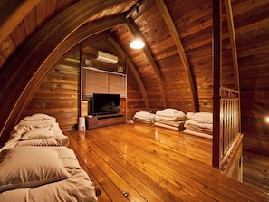 Un dormitorio acogedor en el ático, con paredes de madera, un televisor de pantalla plana y ropa de cama apilada ordenadamente.