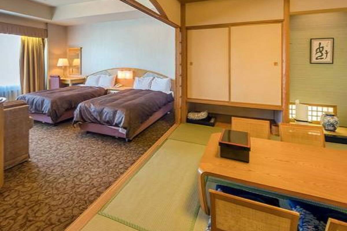A hotel room with two beds, a desk, and a traditional Japanese-style wall.