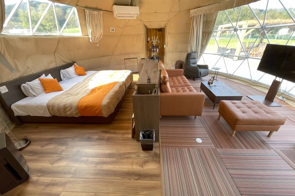 A spacious tented room with a large bed, a sofa, a small table, and a television.