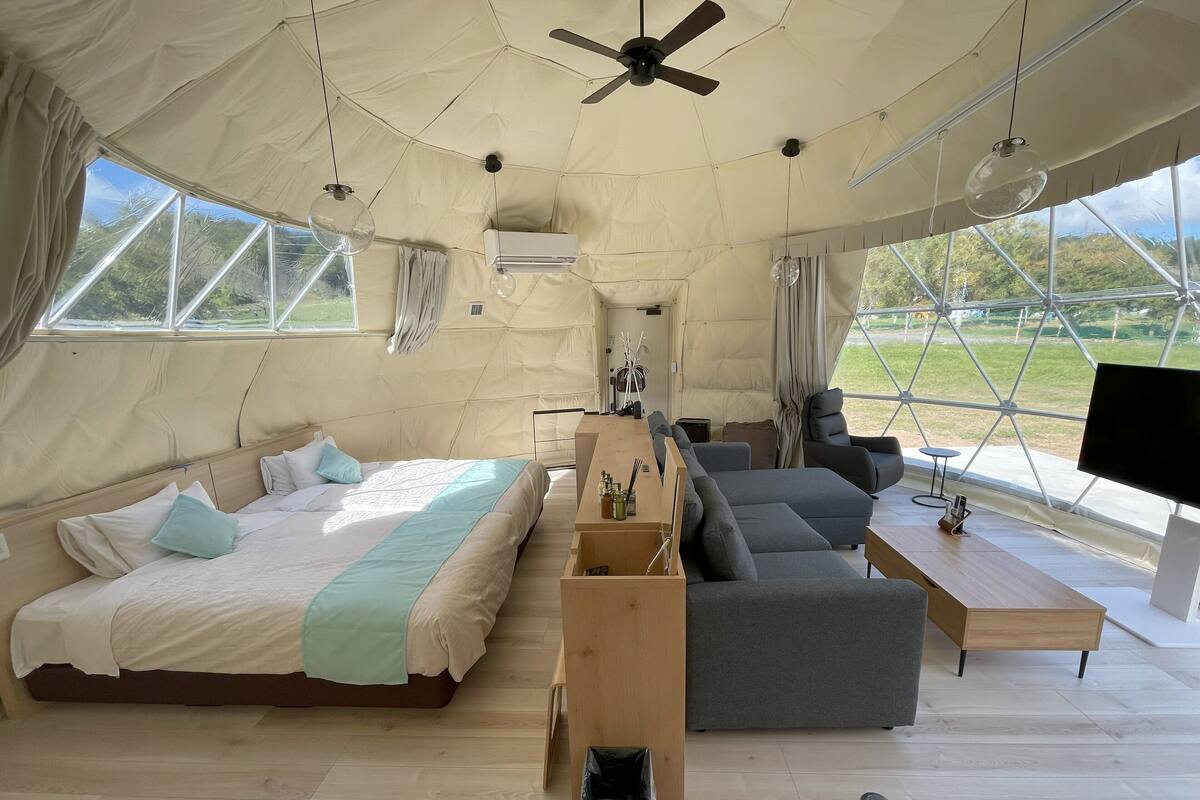A tented accommodation with a bed, sofa, TV, and wooden flooring.