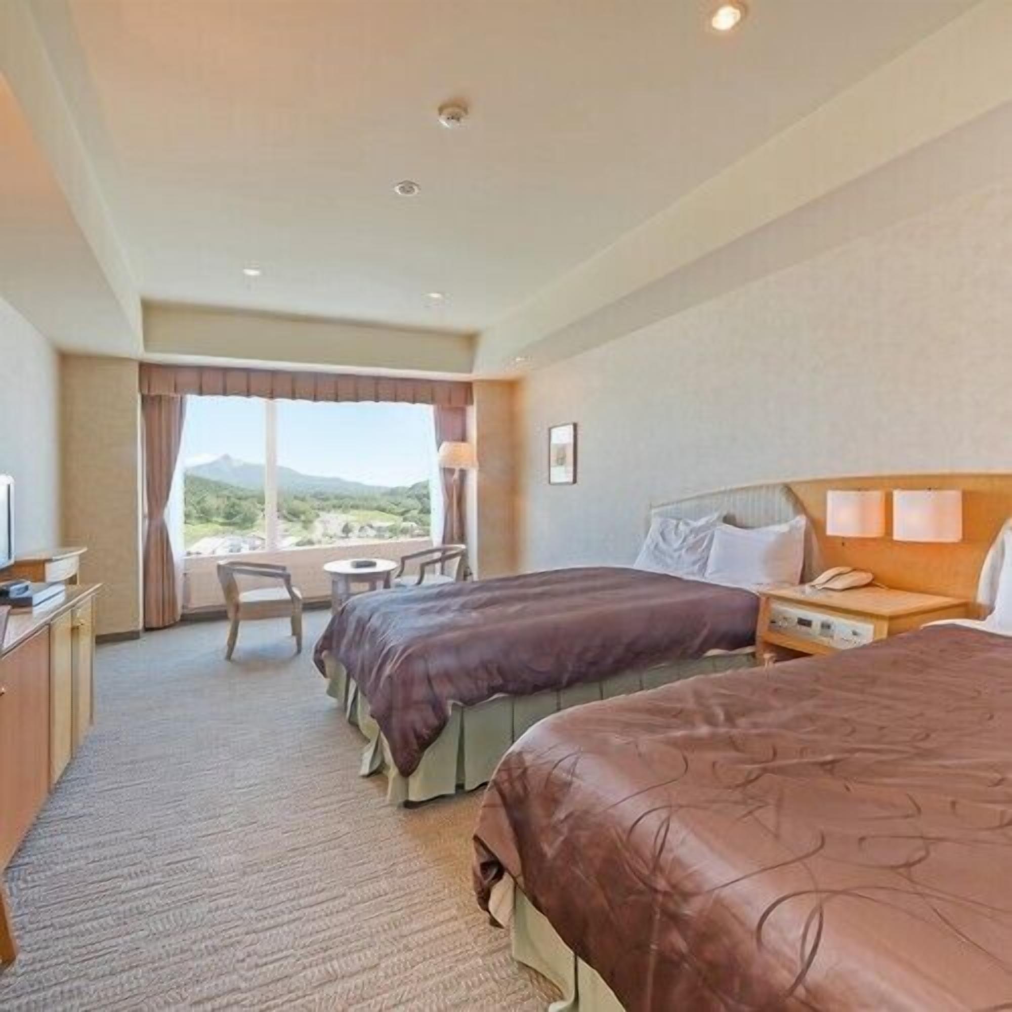 A hotel room with two beds, a desk, a chair, and a view of the outdoors.