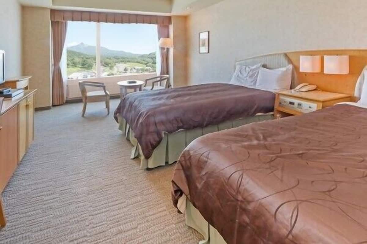 Ein Hotelzimmer mit zwei Betten, einem Schreibtisch, einem Sessel und Blick ins Freie.