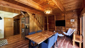 A wooden cabin interior with a dining table, blue chairs, a sofa, a TV, and a staircase. - LiVEMAX RESORT Greenpia Onuma (Mori)