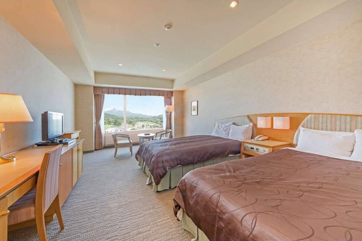 A hotel room with two beds, a desk, a TV, and a view of the outdoors.