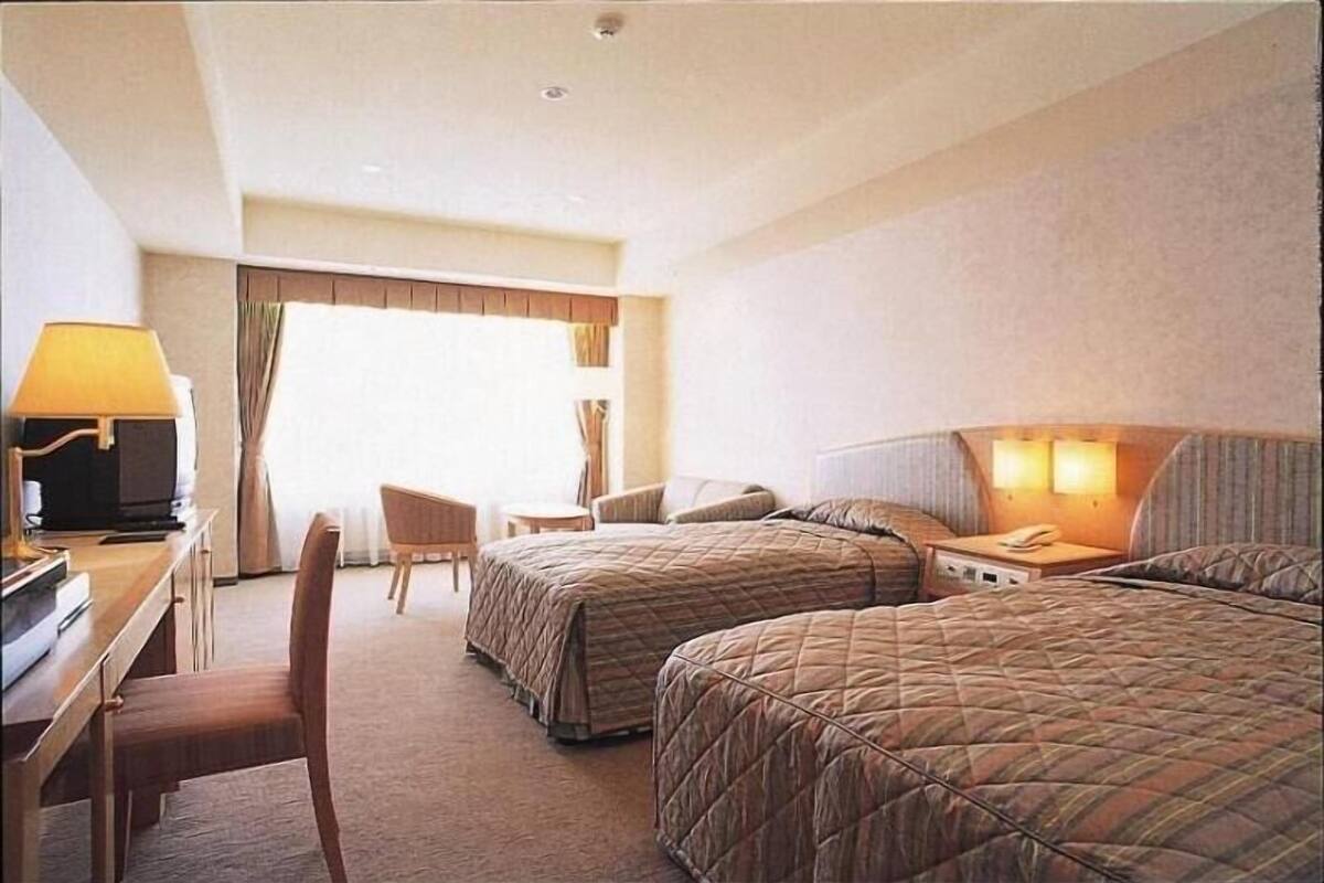 A hotel room with two beds, a desk with a lamp, a chair, and a television.