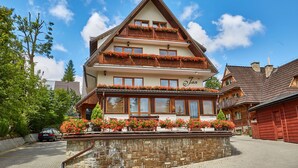 A traditional chalet with a stone facade, wooden balconies, and flower boxes. - Apartamenty Jan (Zakopane)