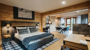 A modern bedroom with a large bed, bedside lamps, a wooden headboard, a dining area with a table and chairs, and a view of the outdoors through a window. - Apartamenty Jan (Zakopane)