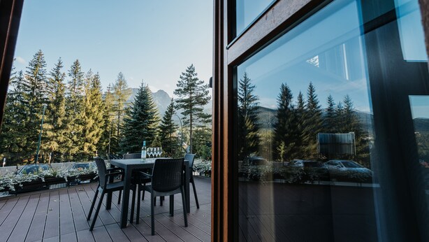 A wooden deck with a table and chairs, overlooking a forest and mountains. - Apartamenty Jan (Zakopane)