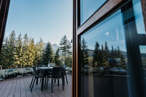 Une terrasse en bois avec une table et des chaises, d’où l’on a une vue sur une forêt et des montagnes.