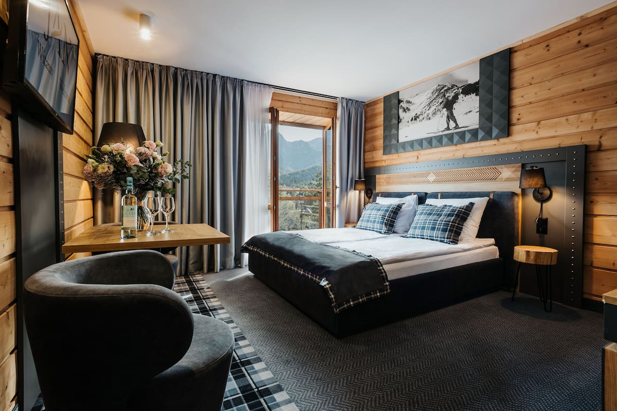 A bedroom with a bed, a desk, a chair, and a view of mountains.