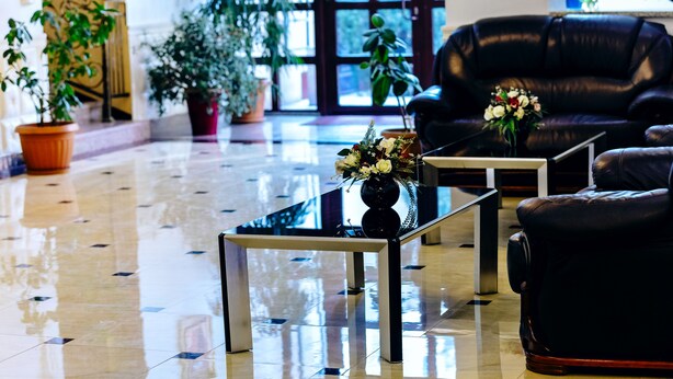 A lobby with a polished floor, a leather sofa, and potted plants. - Grand Hotel (Bishkek)