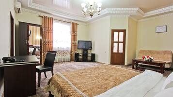 A hotel room with a large bed, a desk with a telephone, a television, and a sofa.