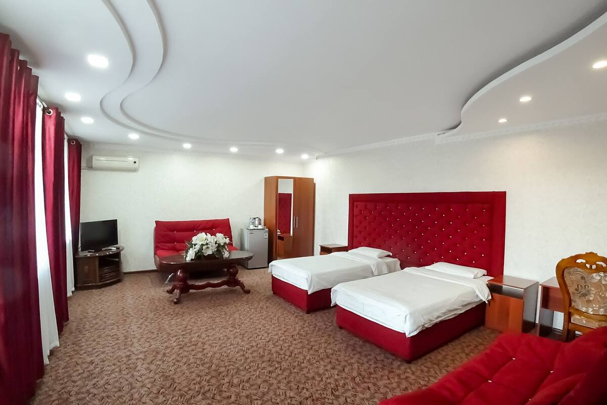 Una habitación de hotel con dos camas, un sofá rojo, un televisor, un escritorio y un armario.