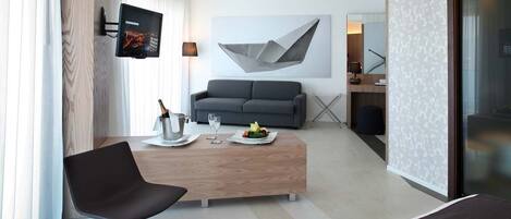 Quarto de hotel moderno com sofá, mesa de centro de madeira, TV fixada na parede e uma grande pintura abstrata.