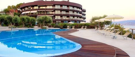 A modern hotel with a circular pool, wooden deck, and lounge chairs.