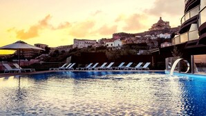Une piscine dotée de chaises longues, d’un élément décoratif aquatique et offrant une vue sur un bâtiment historique situé au sommet d’une colline.