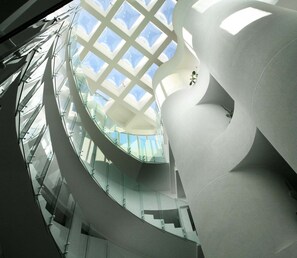 Un intérieur architectural moderne avec un plafond en verre, des murs blancs aux lignes courbes et un escalier en colimaçon.