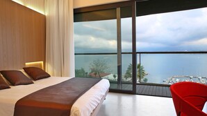 Une chambre avec un grand lit, un fauteuil rouge et une vue sur la mer et le port de plaisance.