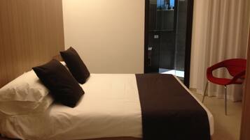 A hotel room with a bed, pillows, a red chair, and a door leading to a bathroom.