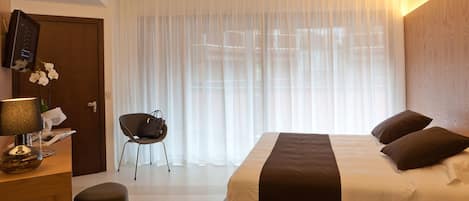 Una habitación de hotel con una cama, una silla, un escritorio con lámpara y un televisor en la pared.