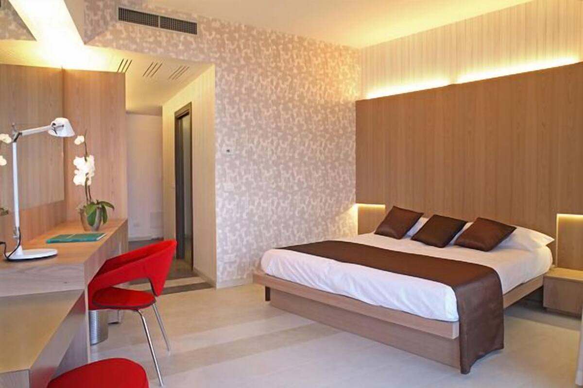 A modern bedroom with a large bed, a desk with a chair, and a mirror.