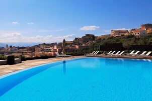 Una piscina en la azotea con sillones de descanso, vistas a un pueblo en la ladera y un cielo despejado.