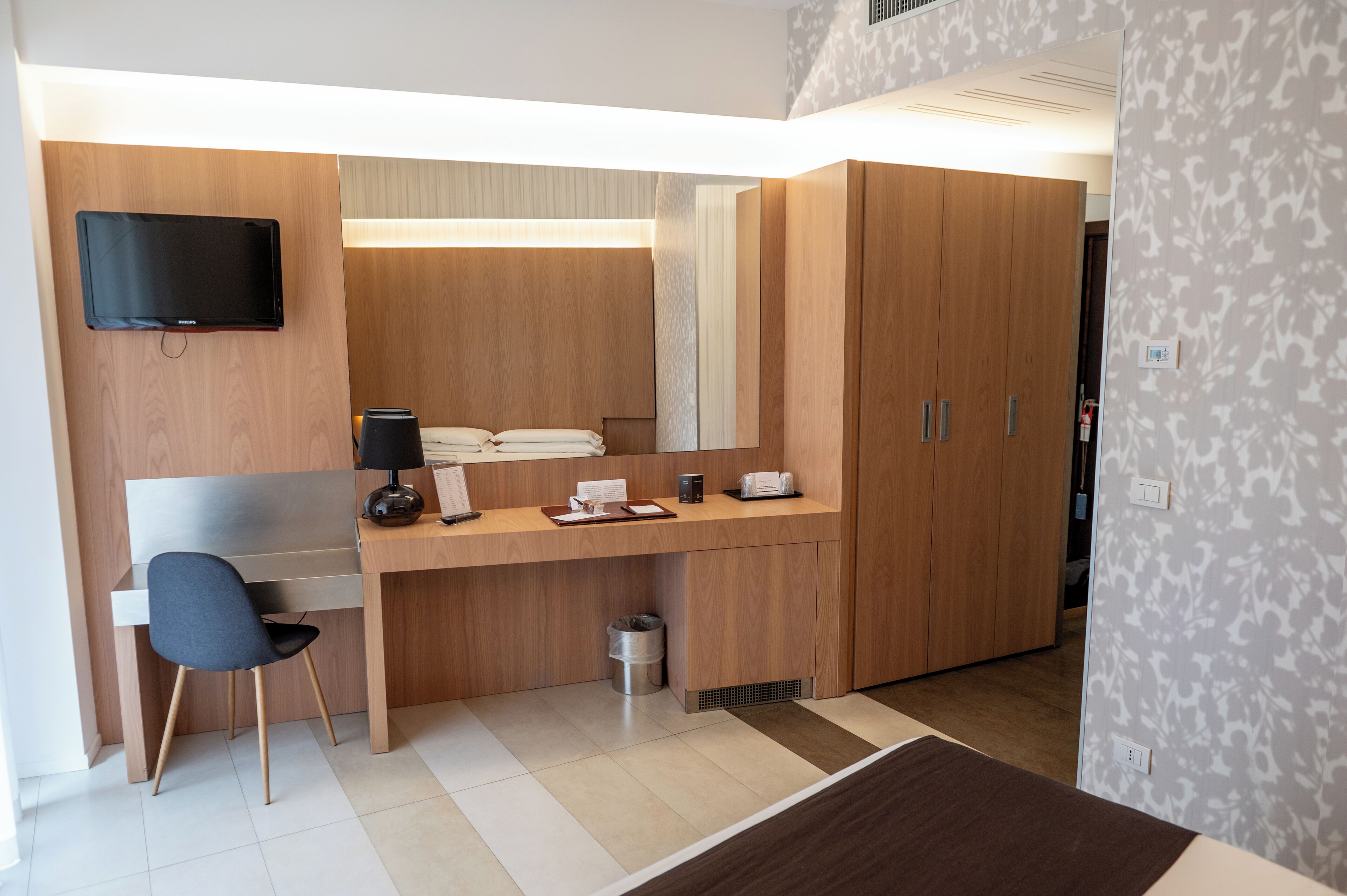Ein modernes Hotelzimmer mit einem Holztisch, einem Flachbildfernseher, einem Sessel und einem Kleiderschrank.
