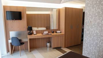 A modern hotel room with a wooden desk, a flat-screen TV, a chair, and a wardrobe.