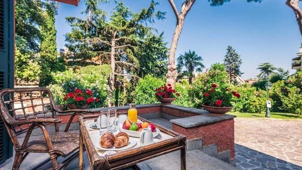 An outdoor breakfast setup with wicker chairs, a table, and a variety of fruits and pastries. - Resort La Rocchetta (Rome)