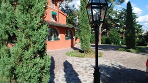 A building with a red facade, a cobblestone pathway, and a street lamp. - Resort La Rocchetta (Rome)
