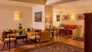 A spacious living room with a sofa set, a coffee table, and a red sofa. There are two lamps, a painting on the wall, and a small table with a vase. - Resort La Rocchetta (Rome)
