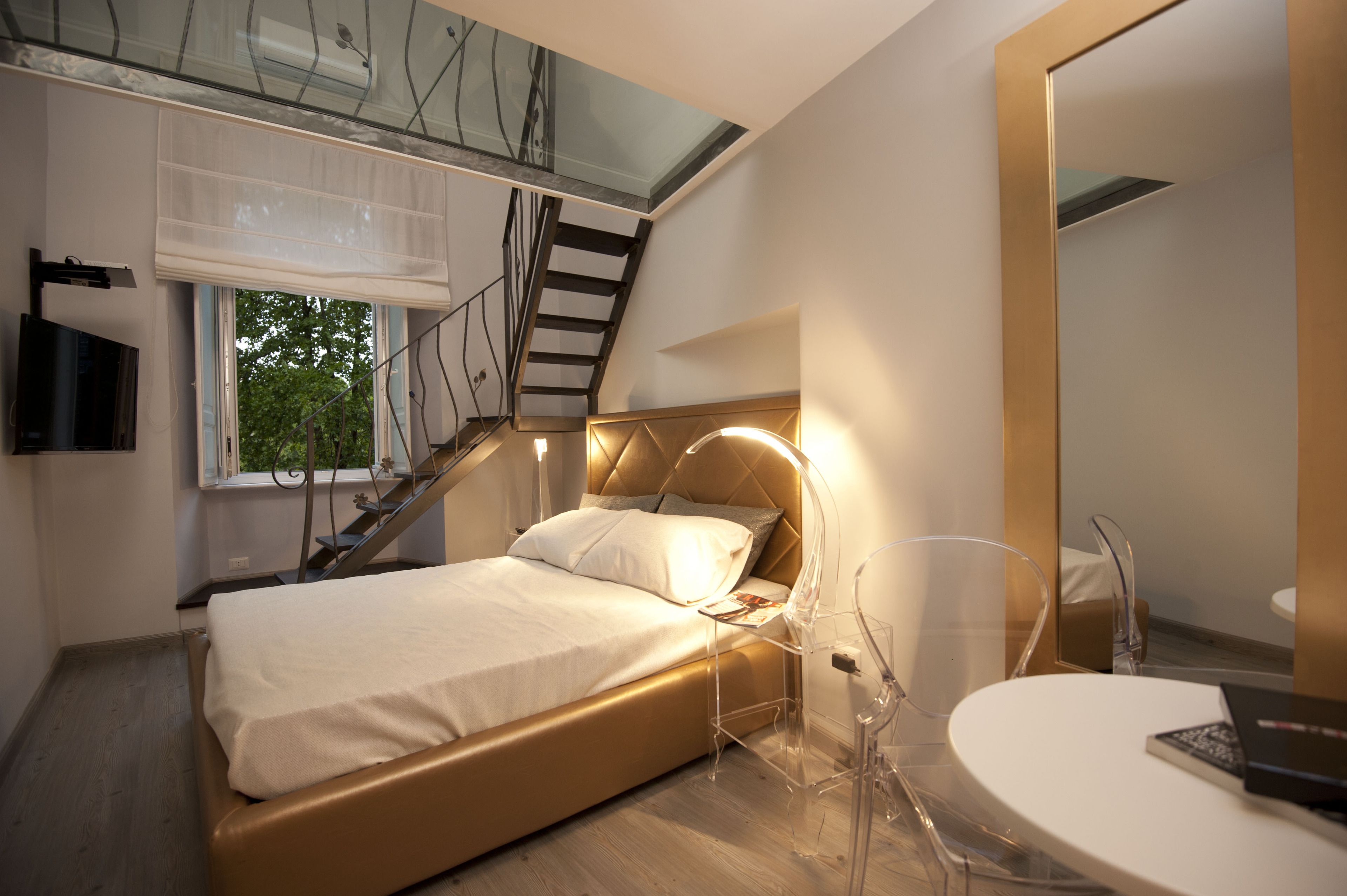 Una camera da letto moderna con un letto, un comodino, una sedia, uno specchio e una scala che conduce a un piano superiore.